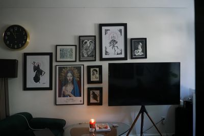 The same gallery wall as in the previous image, this time implemented in a real-life wall over a TV on tripod stand, with a sofa and a glass coffee table visible